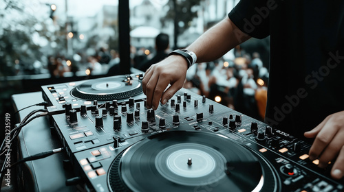 DJ operating a mixing console with a crowd in the background at an outdoor event or party