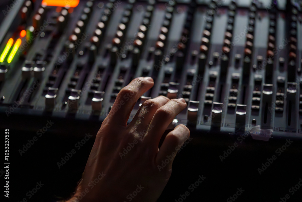 Close-Up of a Hand Operating an Audio Mixing Console in a Dimly Lit Studio, Professional Sound Engineering Setup Close-Up of a Hand Operating an Audio Mixing Console in a Dimly Lit Studio, Professional Sound Engineering Setup