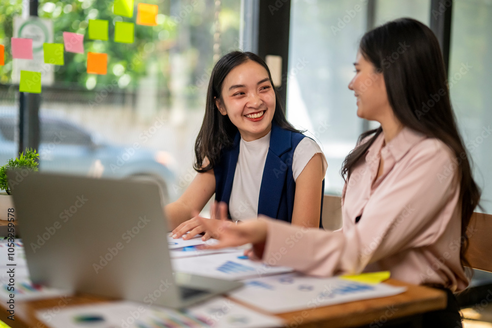 Two women are sitting at a table with a laptop and papers in front of them Two women are sitting at a table with a laptop and papers in front of them