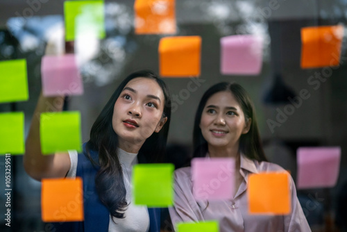 Two women looking at a wall covered in colorful sticky notes