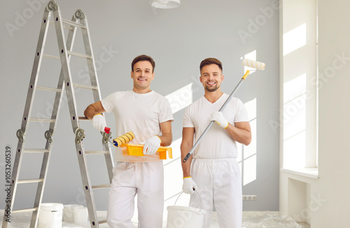 Bild auf Leinwand Portrait of smiling happy team of house painters looking at camera holding paint rollers and going to paint the wall of new apartment