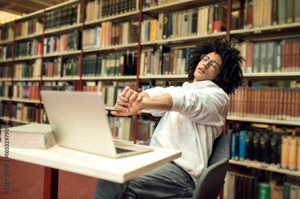 Young man sitting at the laptop in the library and looking tired Young man sitting at the laptop in the library and looking tired