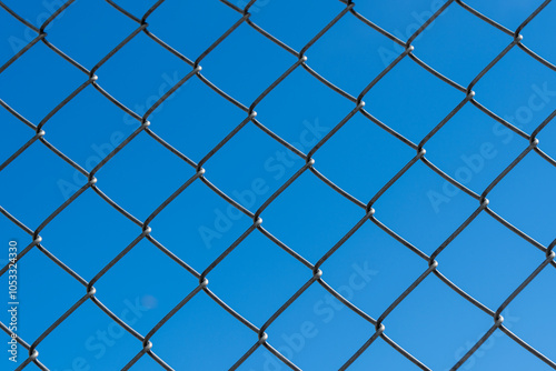 View of cloudless clear blue sky through the cells of a metal wire mesh fence