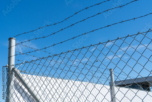Corner of iron fence with mesh and barbed wire against blue sky on sunny day