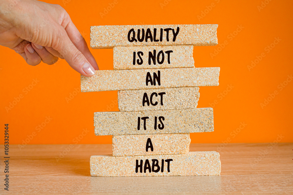 Quality is a habit symbol. Concept words Quality is not an act it is a habit on brick blocks. Beautiful wooden table, orange background. Businessman hand. Business quality is a habit concept.