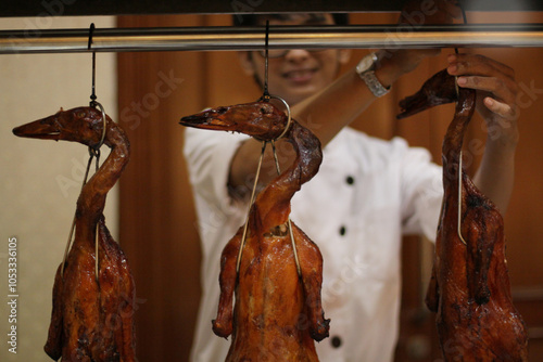 Unidentified male chef holding hanging roasted duck stall at a wedding reception.