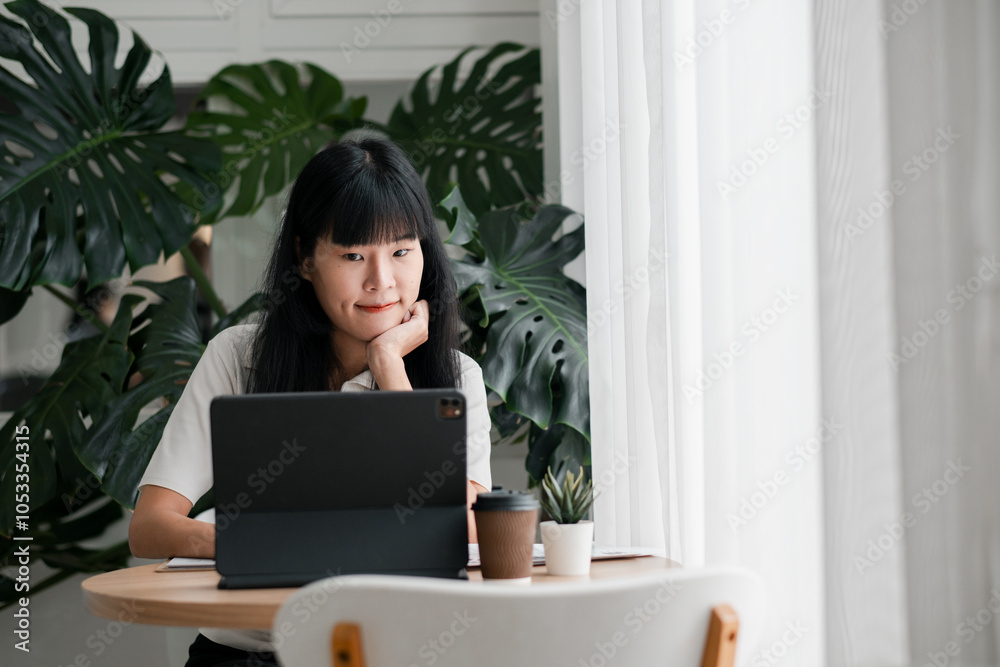 A young woman focused on her tablet in a cozy home office setting, surrounded by lush green plants and soft natural light. A young woman focused on her tablet in a cozy home office setting, surrounded by lush green plants and soft natural light.