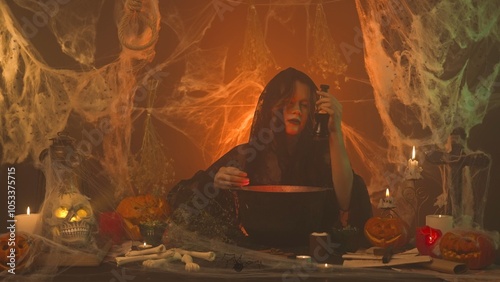 A witch in black clothing conjures up a skull sitting in a scary kitchen with pumpkins and potions. photo