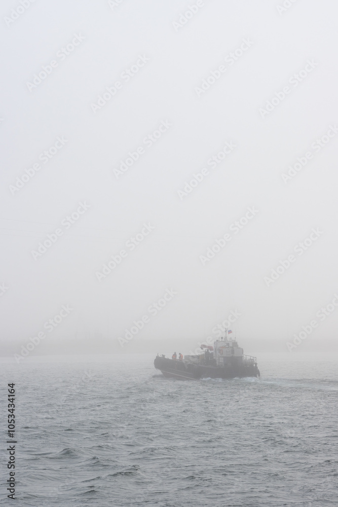 The barge floats on the river in the fog. Water transport by barge. Crossing the river. Transport infrastructure in remote regions of Siberia and the Russian Far East. Foggy weather. Poor visibility. The barge floats on the river in the fog. Water transport by barge. Crossing the river. Transport infrastructure in remote regions of Siberia and the Russian Far East. Foggy weather. Poor visibility.