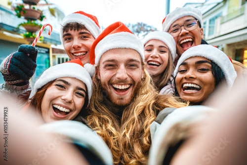 Happy friends wearing santa claus hat taking selfie at Christmas time together on city street - Group of young multi ethnic people having new year party outside - Winter holidays concept photo