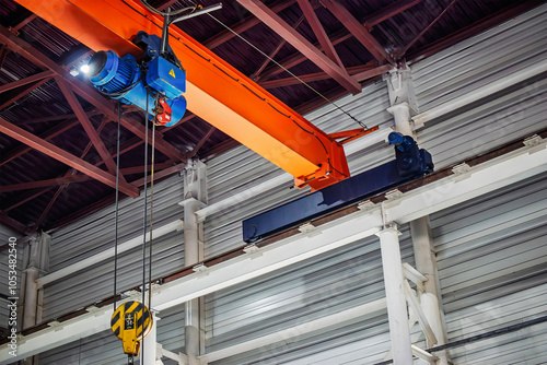 A crane beam with hoist and pulley system suspended from the ceiling of an industrial workshop, designed for heavy lifting and movement