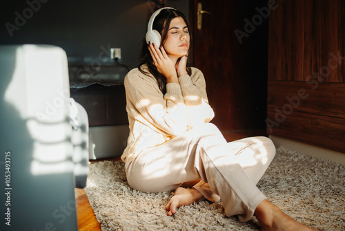 Young caucasian woman enjoying music on wireless headphones at home	 photo