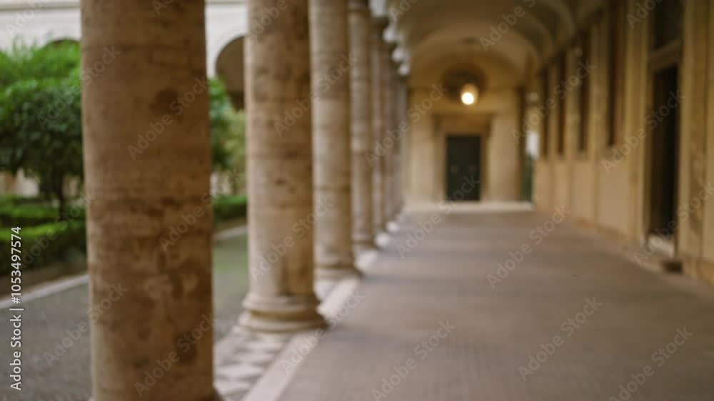 Defocused view of an old university campus corridor featuring classical architecture with stone columns and arches surrounded by lush greenery outdoors. Defocused view of an old university campus corridor featuring classical architecture with stone columns and arches surrounded by lush greenery outdoors.