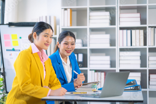 Two Asian businesswomen are deeply engaged in a discussion about data analysis work on a computer screen with graphs and charts. Showcase teamwork