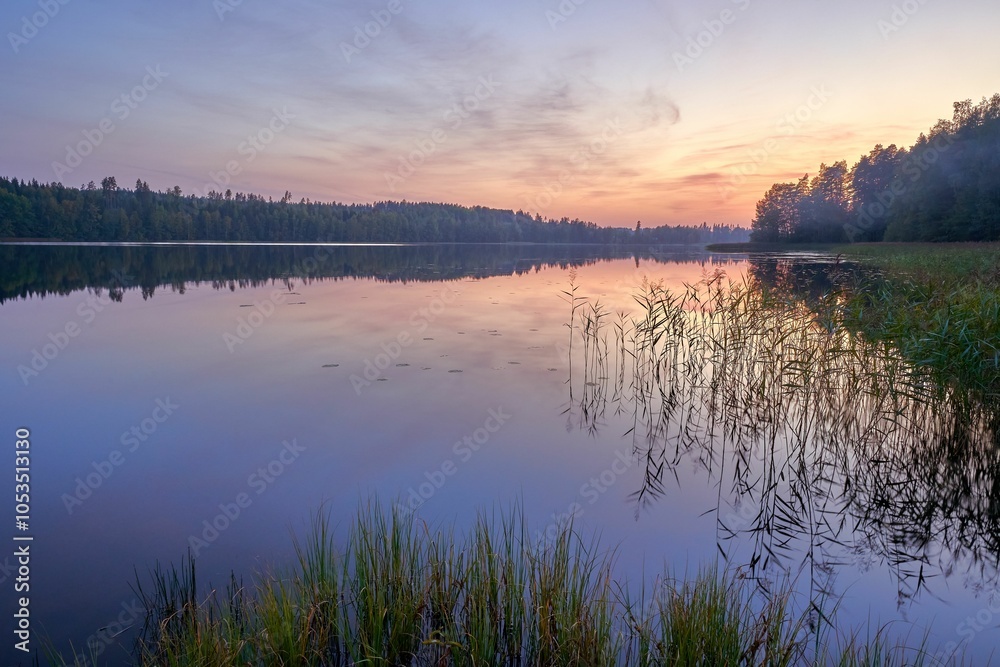 Fototapeta premium Sunset over a tranquil lake with forest reflections.