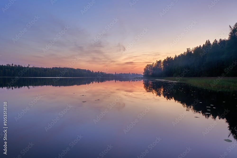 Obraz premium Sunset over a tranquil lake with forest reflections.