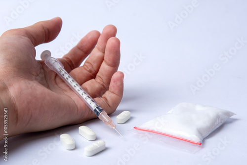 hand trying to reach and use drugs on white table with syringe, methamphetamine, and pills. The concept for drugs addiction, International Day against Drug Abuse. say no to drugs