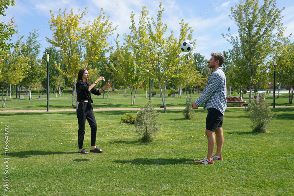 A couple is actively engaged in a game of volleyball, laughing and enjoying their time together in a bright, sunny park filled with trees and open space A couple is actively engaged in a game of volleyball, laughing and enjoying their time together in a bright, sunny park filled with trees and open space