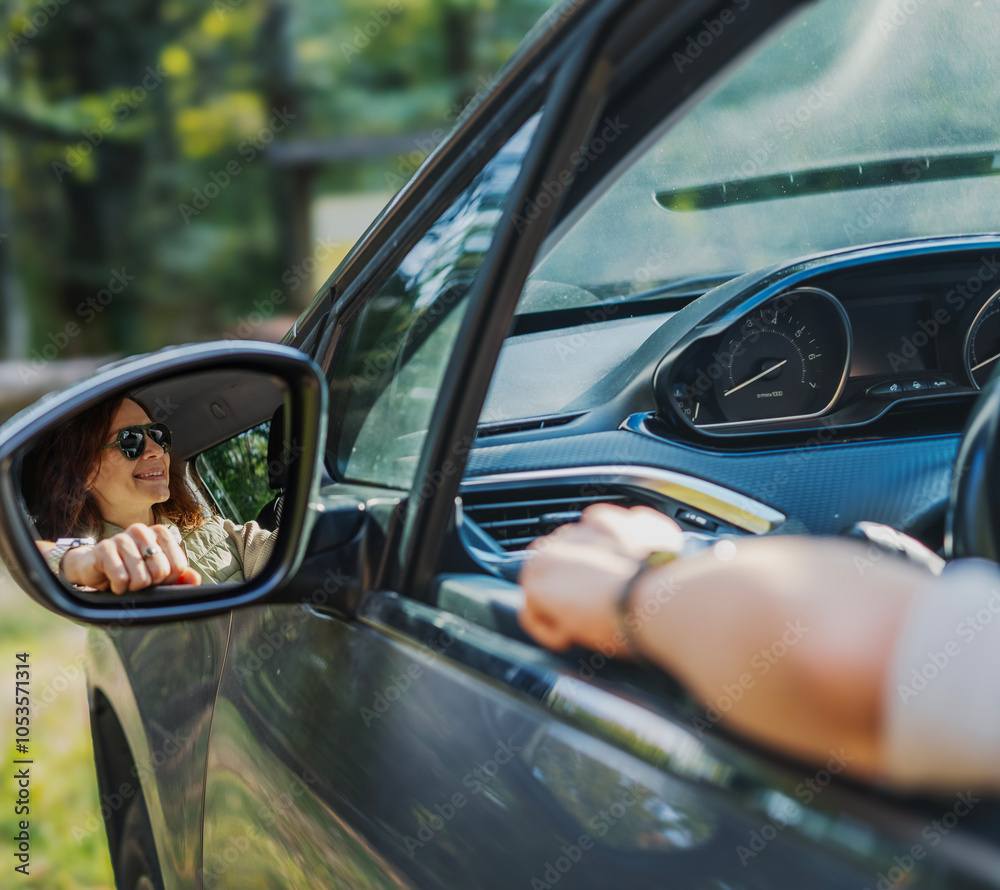 Reflection of happy in side mirror of car young woman driver sitting behind the wheel of car