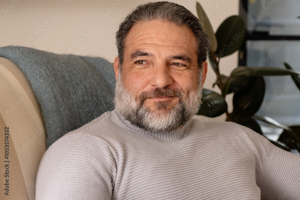 Fototapeta premium Smiling mature man relaxing at home, enjoying peaceful moment on sofa
