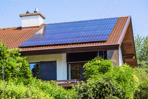 Solar Panels on Red Tile Roof of Old House with Green Garden Landscaping. Modern Solar Panel Station on Roof House.
