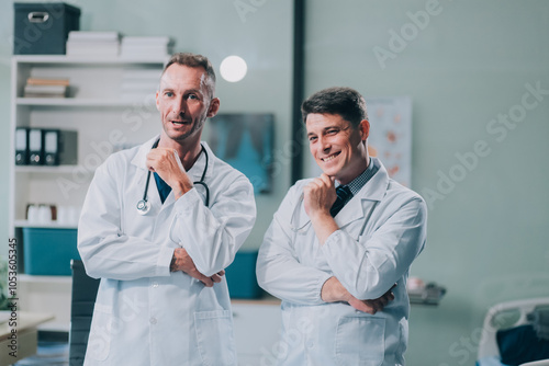 Portrait of two dedicated doctors smiling and looking at camera while holding a tablet and a diary in clinic. Two smiling doctors in white coat working in an office and looking at camera.