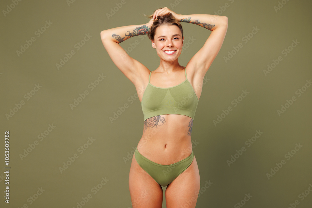 Fototapeta premium Young smiling happy nice lady woman with slim skinny body perfect skin she wear top bra lingerie stand hold hair raise up hands isolated on plain pastel green background. Lifestyle diet fit concept.