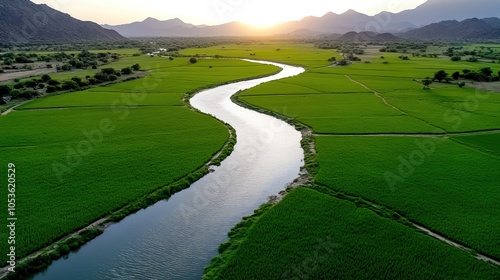 A serene landscape featuring a winding river surrounded by lush green fields and distant mountains under a setting sun.