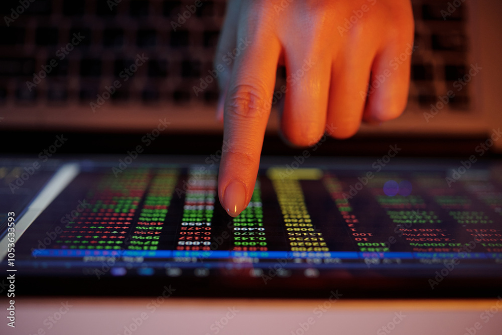 Close-up of a hand interacting with a tablet screen displaying colorful financial data charts against a dimly lit background