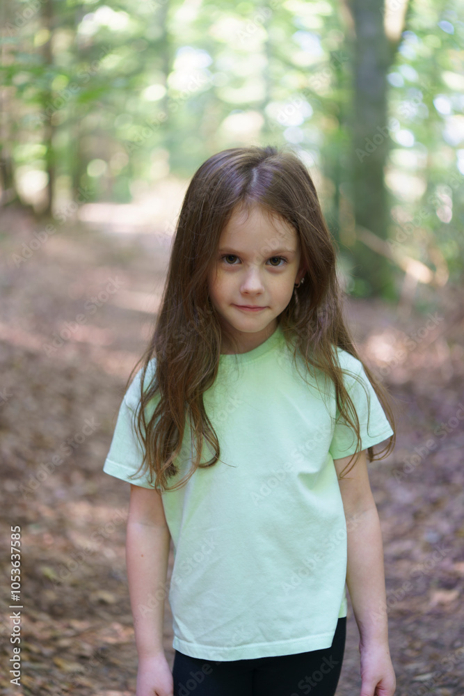 Little girl in green t-shirt stands alone in forest among trees. Concept of unity with nature, childhood and loneliness Little girl in green t-shirt stands alone in forest among trees. Concept of unity with nature, childhood and loneliness