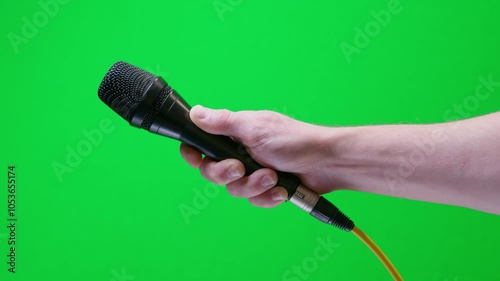 Newscaster’s hand thrusts a reporter’s microphone into frame, close-up shot against chroma green backdrop.