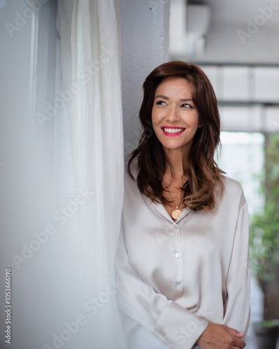 Smiling mid aged woman standing at the wall and looking out of the window