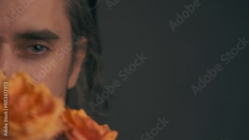 Captivating Allure  - Slavic man long hair an unshaven face hides half of his face with orange roses. He winks and smiles with his eyes, then removes the bouquet, revealing his cheekbones photo