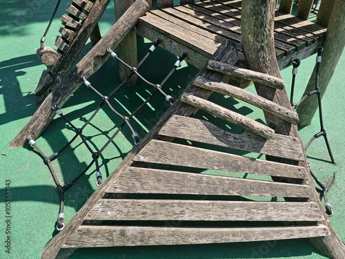 Un ensemble de rampes en bois et de filets en corde est intégré à une structure de jeu sur un sol en caoutchouc vert, offrant aux enfants un défi d'escalade stimulant et sûr dans un cadre naturel. photo