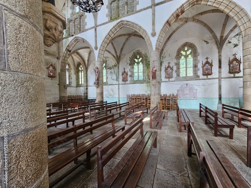 Des rangées de bancs en bois remplissent l'intérieur de l'église, entourées par des murs en pierre ornés de statues et de stations du chemin de croix, avec de grandes arches et des vitraux photo