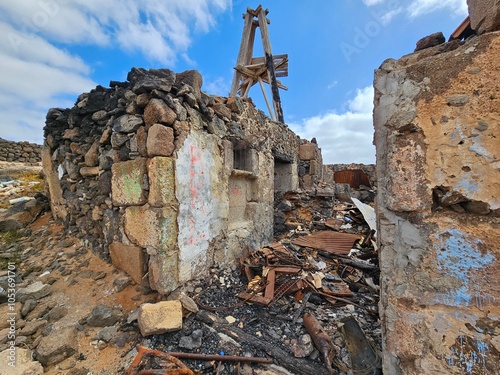 Les ruines d'une ancienne structure en pierre, partiellement effondrée, avec des murs marqués de graffitis et des débris métalliques éparpillés au sol, sous un ciel partiellement nuageux à Arrecife photo