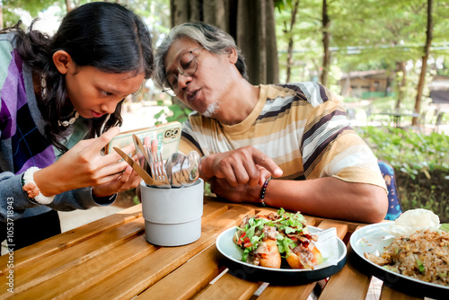 Southeast Asian father teaching his teenage daughter foodgraphy at an outdoor restaurant photo