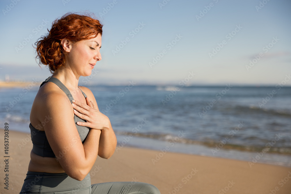 Red-haired woman sitting on the sand doing meditation early in the morning Red-haired woman sitting on the sand doing meditation early in the morning