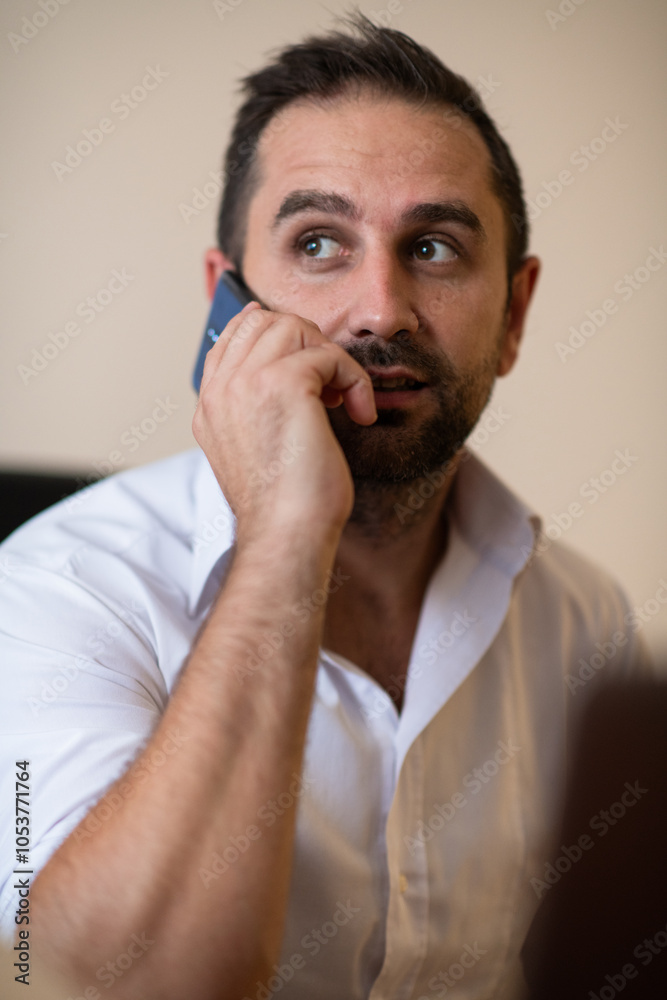 A businessman talking on his smartphone while seated in an office, showcasing his professional demeanor and active communication. A businessman talking on his smartphone while seated in an office, showcasing his professional demeanor and active communication.