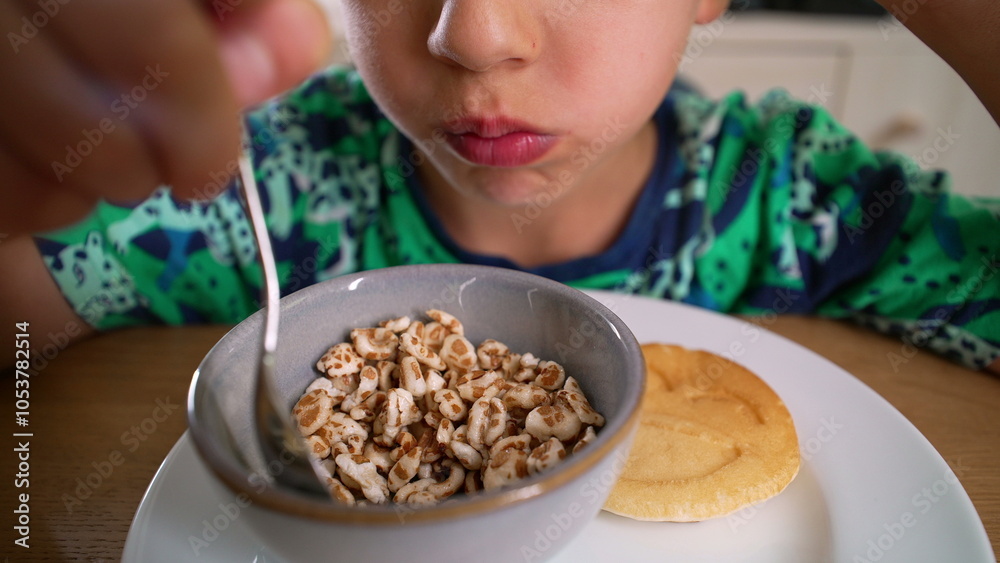 Young Boy eating cereal from a bowl, lifting the spoon to his mouth. A pancake sits on the plate, a simple and casual breakfast moment Young Boy eating cereal from a bowl, lifting the spoon to his mouth. A pancake sits on the plate, a simple and casual breakfast moment