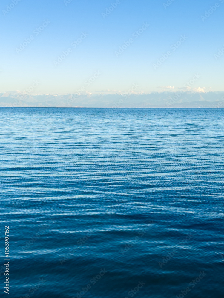 Obraz premium Issyk-Kul Lake with a cloudy sky and mountains in the background. The water is calm, reflecting the sky. The serenity and peacefulness of nature in the early morning hours.