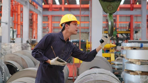 Factory worker operating crane hook for metal coils