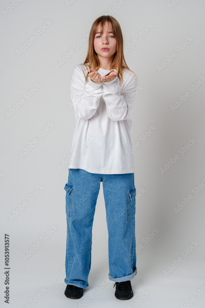 Young woman in white long-sleeve shirt blowing a kiss against a plain background