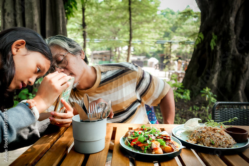 Southeast Asian father teaching his teenage daughter how to become a good foodgrapher at an outdoor restaurant photo