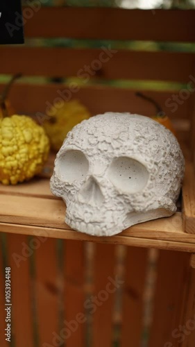 A close-up of a decorative skull with intricate floral carvings, sitting on a wooden shelf, accompanied by autumn gourds. Perfect for Halloween or Day of the Dead displays. Vertical video. photo