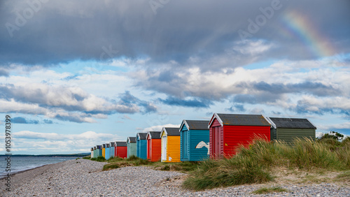 Strandhütten bei Findhorn Beach, Drohnenaufnahme mit Meer im Vordergrund, weiße Wolken am blauen Himmel bei tiefstehender Sonne photo