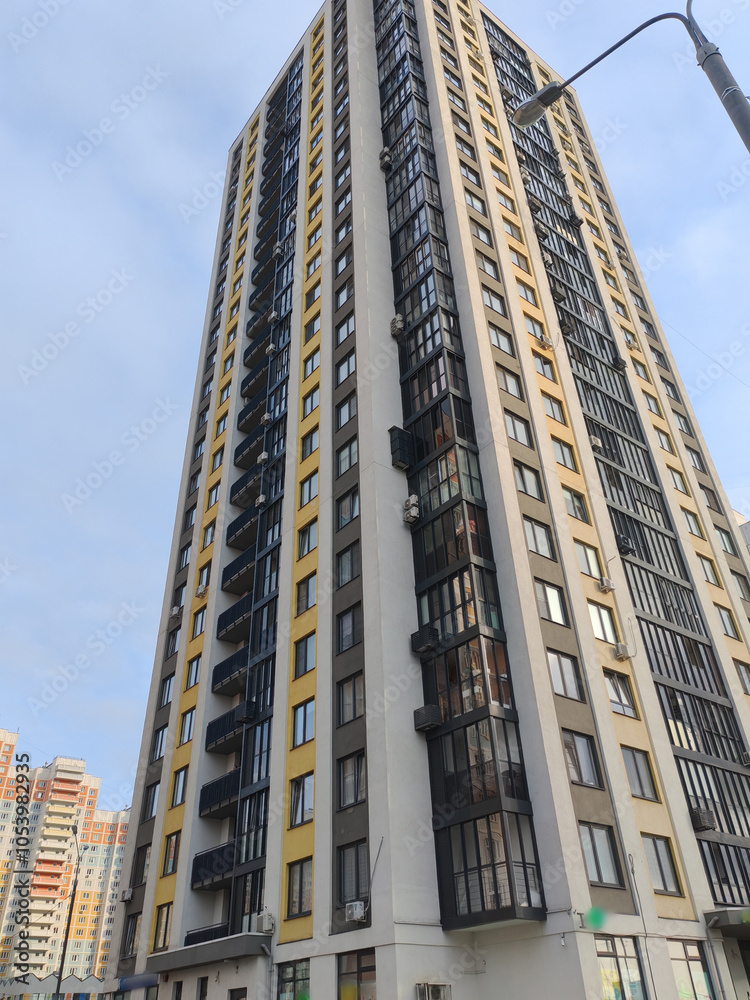 Fototapeta premium A towering residential building with pastel accents, featuring a wide array of windows and balconies. The design reflects the contemporary urban approach to high-density living in city environments.