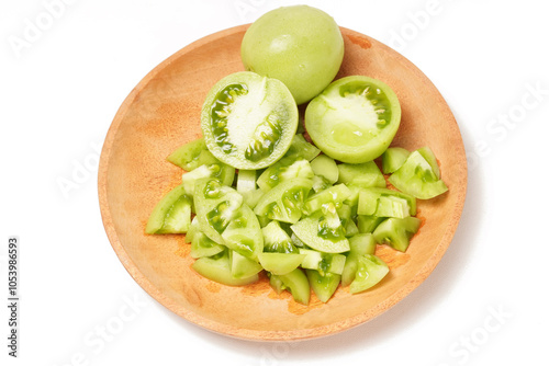 Whole and sliced green tomatoes (Solanum lycopersicum) on a wooden plate against a white background. The photo captures the fresh, juicy, and crisp texture of the slices.