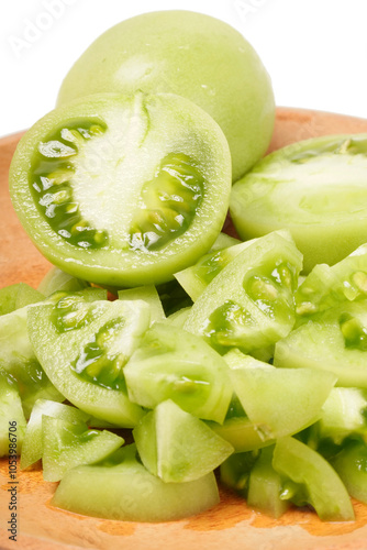 Whole and sliced green tomatoes (Solanum lycopersicum) on a wooden plate against a white background. The photo captures the fresh, juicy, and crisp texture of the slices.