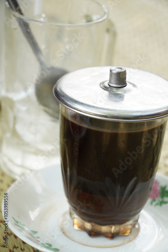 A glass of strong black coffee (Coffea arabica) with grounds, served on a saucer due to heat. Enjoy hot or with ice once cooled. A beloved drink among Indonesians.